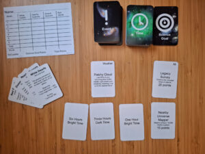 Three decks of cards marked event, time and science goal. Several cards lie face up alongside a scoresheet